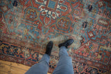 Feet on an antique Persian Heriz carpet, showcasing geometric patterns and wear to foundation.