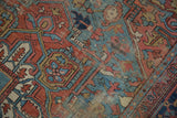 Antique Heriz carpet: geometric floral motifs, cherry red, sky blue, and exposed foundation.