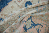 Folded vintage distressed Oushak carpet, indigo blue, dusty rose, and ivory palmette motifs.