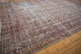 Distressed vintage Khorassan rug corner with red, ivory floral patterns, and fringe.