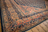 Angled view of a vintage Lilihan carpet's corner with dusty blush borders and a navy Herati field.