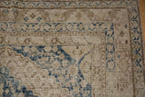 Vintage distressed Khotan rug corner showing blue floral motifs, pawn border design, and visible foundation.