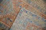Distressed Karaja rug corner folded, showing worn pale red, blue, beige patterns and foundation.