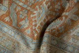 Distressed Heriz runner's folded pile, showing faded terra cotta, blue, and beige geometric design.