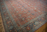 Angled view of a distressed Bijar carpet with a soft ruby red field and detailed powder blue border.