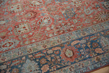 Detailed view of a distressed Persian rug's even wear and its soft ruby red and powder blue floral motifs.