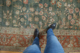 Distressed Sarouk carpet detail: playful green field, rust border, and worn floral texture.