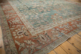 Distressed Sarouk carpet corner with textured rust border and deep green floral field.