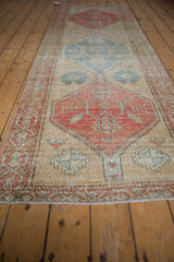 Distressed vintage Persian runner detail: pale cherry red medallion, worn pile, and faint foundation.
