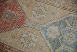 Distressed Northwest Persian rug showing worn texture, serrated contour in pale red, beige, teal.