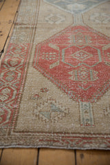 Distressed vintage Northwest Persian runner, showing worn beige field and faded cherry red geometric patterns.