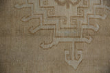 Close-up of distressed Oushak rug pile, showing geometric hook and latch motifs in beige.