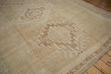 Distressed beige Oushak rug with meandering vine border and intact side selvage.