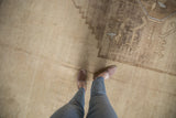 Distressed vintage Oushak carpet with abrashed beige field and muted geometric motifs.