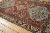 Distressed Hamadan rug corner with chestnut field, ivory border, serrated leaf motif.