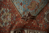 Folded close-up of Vintage Distressed Hamadan rug, featuring geometric lattice, chestnut, and denim blue.