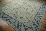 Angled view of a vintage Oushak rug's navy palmette border and low-pile beige field.