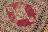 Antique Persian Kerman rug detail showing ivory millefleur border, worn cochineal red field, and fringed edge.