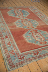 Vintage distressed Caucasian rug showing abrashed cinnabar red field and serrated blue border.
