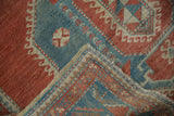 Folded corner of vintage distressed Caucasian rug with serrated leaf border and visible knot heads.