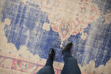 Distressed vintage Oushak carpet showing worn blue pile, exposed foundation, and faded red border.