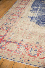 Distressed vintage Oushak carpet corner with faded blush red palmette border and royal blue patterns.
