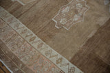 Distressed Oushak carpet texture with abrashed coffee brown field and pale blush border.