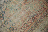 Antique Kerman carpet showing worn texture, dusty teal and pale red floral patterns.
