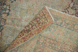 Distressed Kerman carpet pile reveals wear, intact side selvage, and faded dusty teal, red patterns.