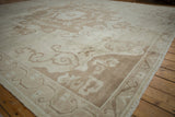 Vintage distressed Oushak rug showing its curvilinear patterns and border in muted ivory and coffee brown hues.