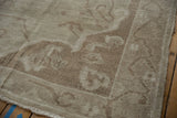 Distressed Oushak rug corner, showing muted beige pile, subtle pattern, and fringe.