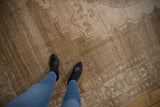 Distressed vintage Oushak carpet, its abrashed sand and beige field highlighted by boots.