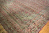 Distressed Kerman rug corner, showing millefleur patterns with worn raspberry, ivory, and denim blue hues.