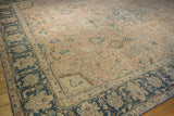 Distressed vintage Tabriz rug corner showing worn dusty blush field and intricate navy border.