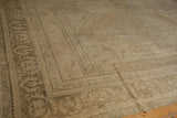 Distressed Oushak rug corner, revealing faded beige pile and muted pillared border design.