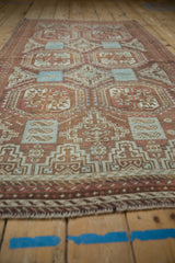 Distressed Belouch rug's geometric guls in faded raspberry, chestnut, and powder blue pile.