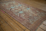 Distressed Belouch rug's geometric guls, faded raspberry and blue, with wear revealing foundation.