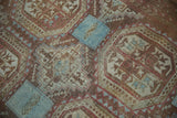 Distressed Belouch rug close-up: faded raspberry and blue geometric motifs with visible worn pile.