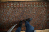 Distressed vintage Belouch rug with geometric panels, worn texture, and faded earthy tones.