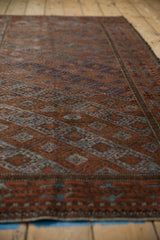 Distressed vintage Belouch rug with diagonal lattice and floral geometric motifs in chestnut and blue tones.