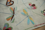 Embroidered dragonfly motifs in blue, green, and orange on a plain woven kilim.