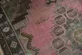Weaver's signature woven into the distressed, abrashed pink field of a vintage Kars rug.