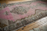 Angled view of a vintage Kars runner's distressed, low pile and abrashed blush pink field.