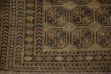 Lower corner of a distressed Afghani rug, with dusty gold guls, brown borders, navy accents, and fringe.
