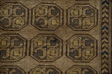 Distressed Afghani rug close-up: geometric guls with inverted coloration in dusty gold, coffee brown.