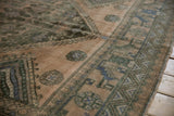 Distressed vintage Shiraz carpet border showing geometric arabesques in muted green and blue tones.