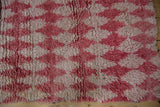 Thick wool pile and visible knot heads of a Moroccan rug in raspberry and ivory.