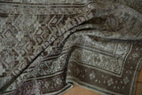 Distressed texture on a vintage Caucasian runner with geometric motifs in soft brown and mauve tones.