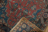 Vintage Heriz rug corner, showing madder red field, blue floral design, and hand-knotted beige foundation with fringe.