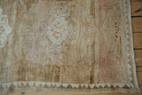 Distressed vintage Kars carpet corner showing even wear across knot heads, pale brown, rose, and chevron zigzag border.